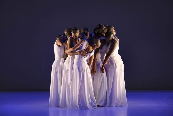 Dancers in white dresses huddle together on a stage