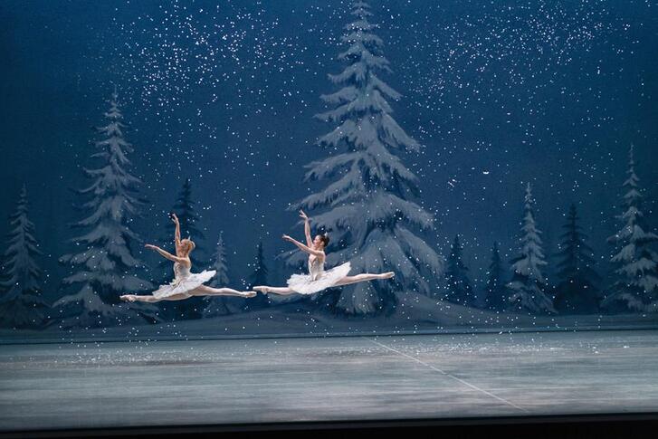 Two ballerinas soaring in the air in front of a winter stage set
