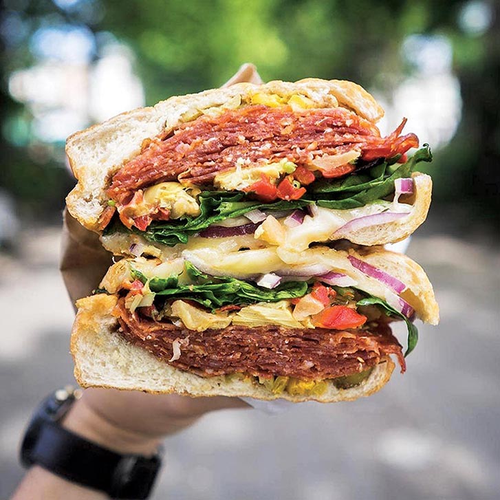 A hand holding a huge sandwich stacked with veggies and meats. 