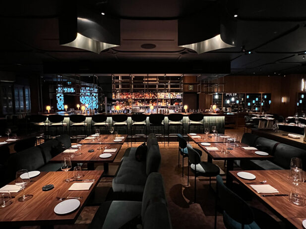 A dark-lit chic restaurant interior with an open kitchen.