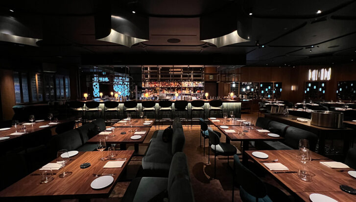 A dark-lit chic restaurant interior with an open kitchen. 