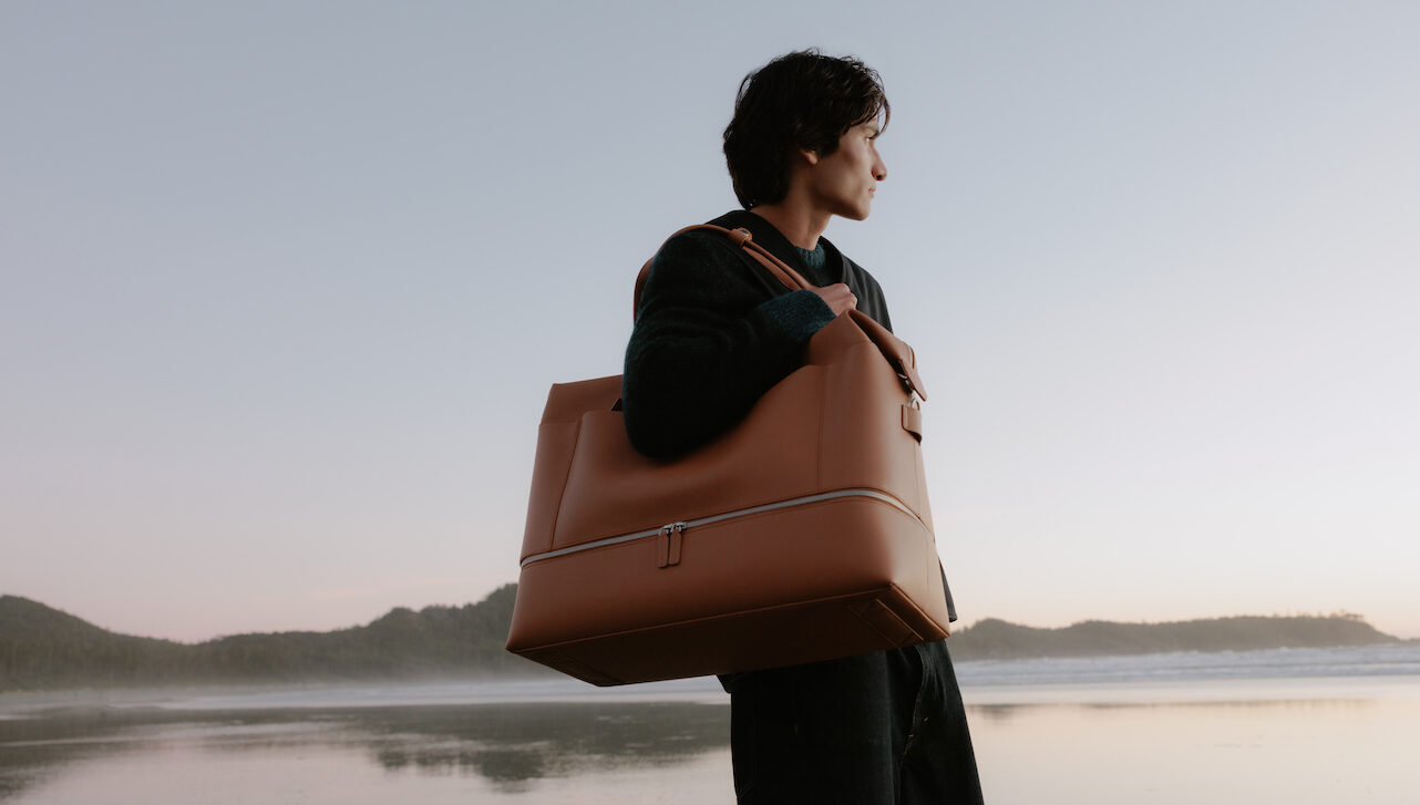 Person carrying Monos bag on a beach.