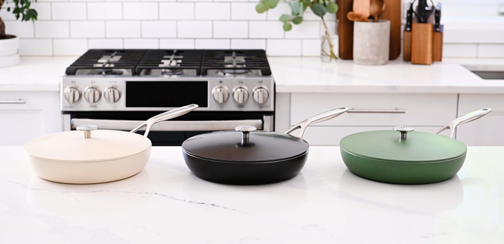 Three pans on a marble kitchen counter in green, cream and black