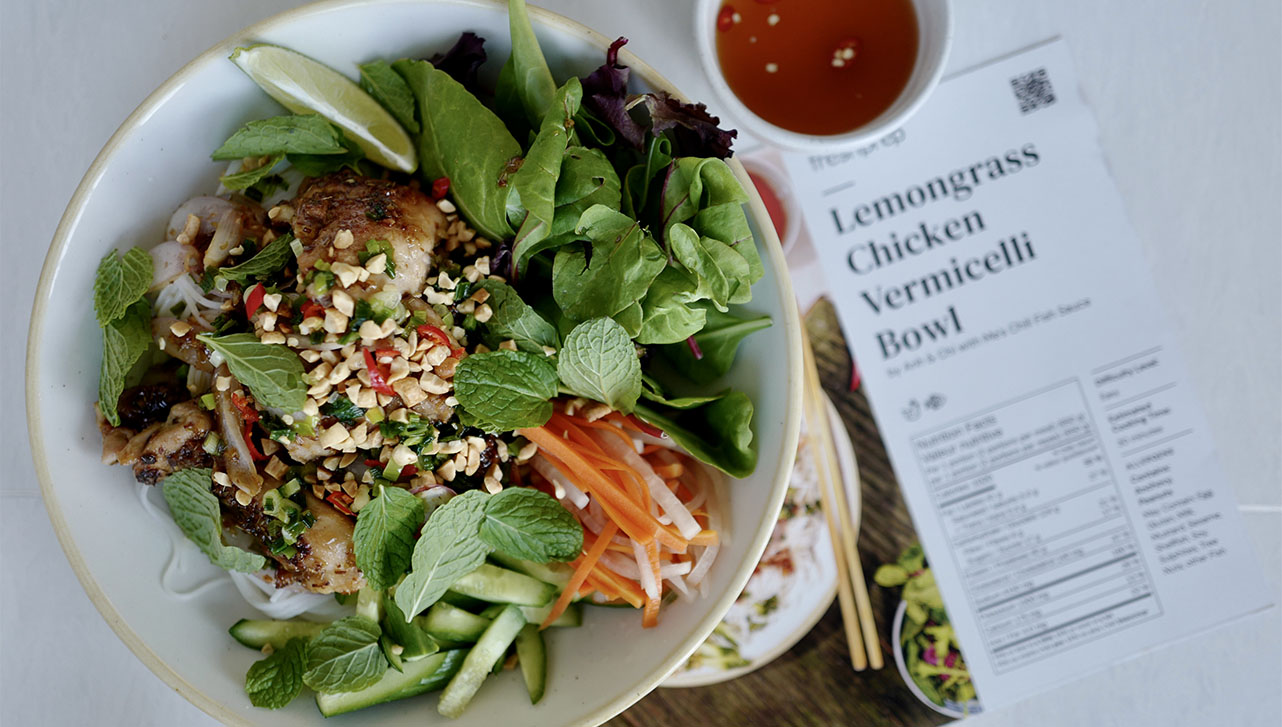 A bowl of lemongrass chicken vermicelli with a recipe to the side of it. 