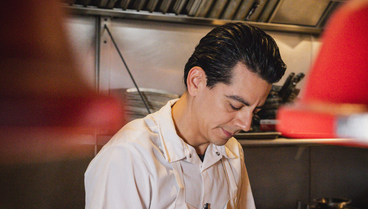 A dark haired chef prepares food in his white uniform.