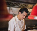 A dark haired chef prepares food in his white uniform.
