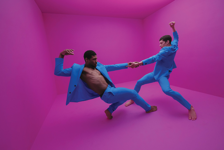 two dancers in blue suits strike a dramatic pose in a bright purple room