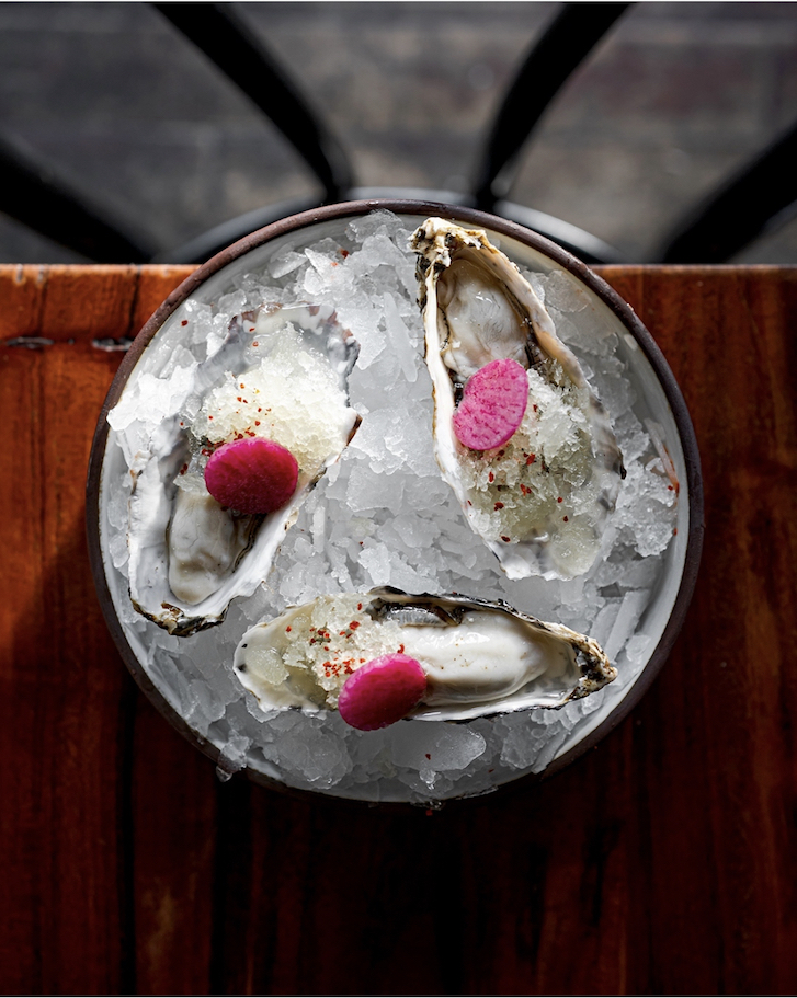 Three oysters with pink pickle garnish on a bowl of ice.