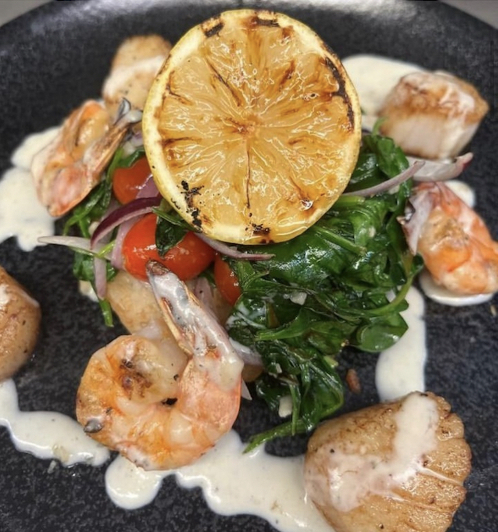Dish with greens in the centre, surrounded by shrimp and scallops.
