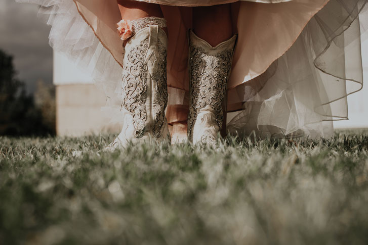 Close up photo of a bride wearing cowboy boots under her wedding dress