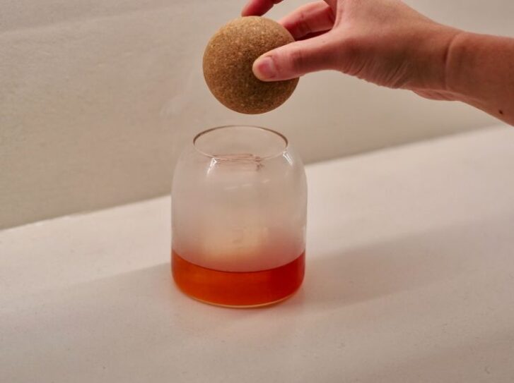 Cocktail in a glass with a hand holding something overtop. 