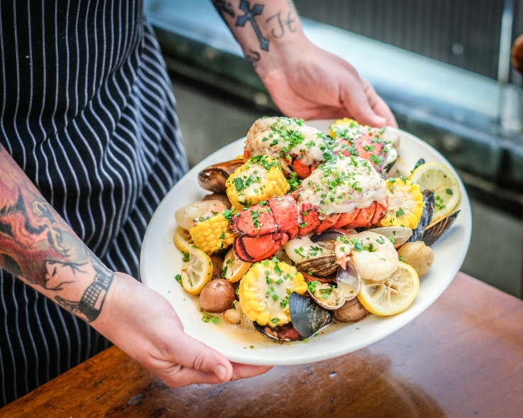 hands holding a plate of seafood, potatoes