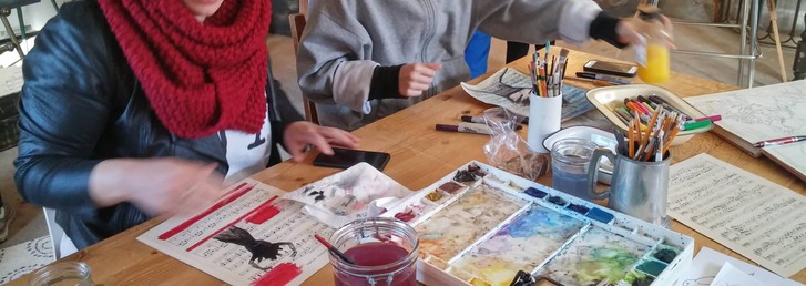 People doing art on a table, with paints, paper and art supplies