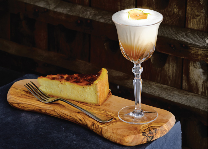Cocktail on wooden board with cheesecake next to it
