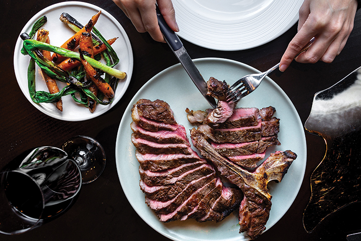Steak being sliced at Elisa, served with vegetables and a glass of red wine