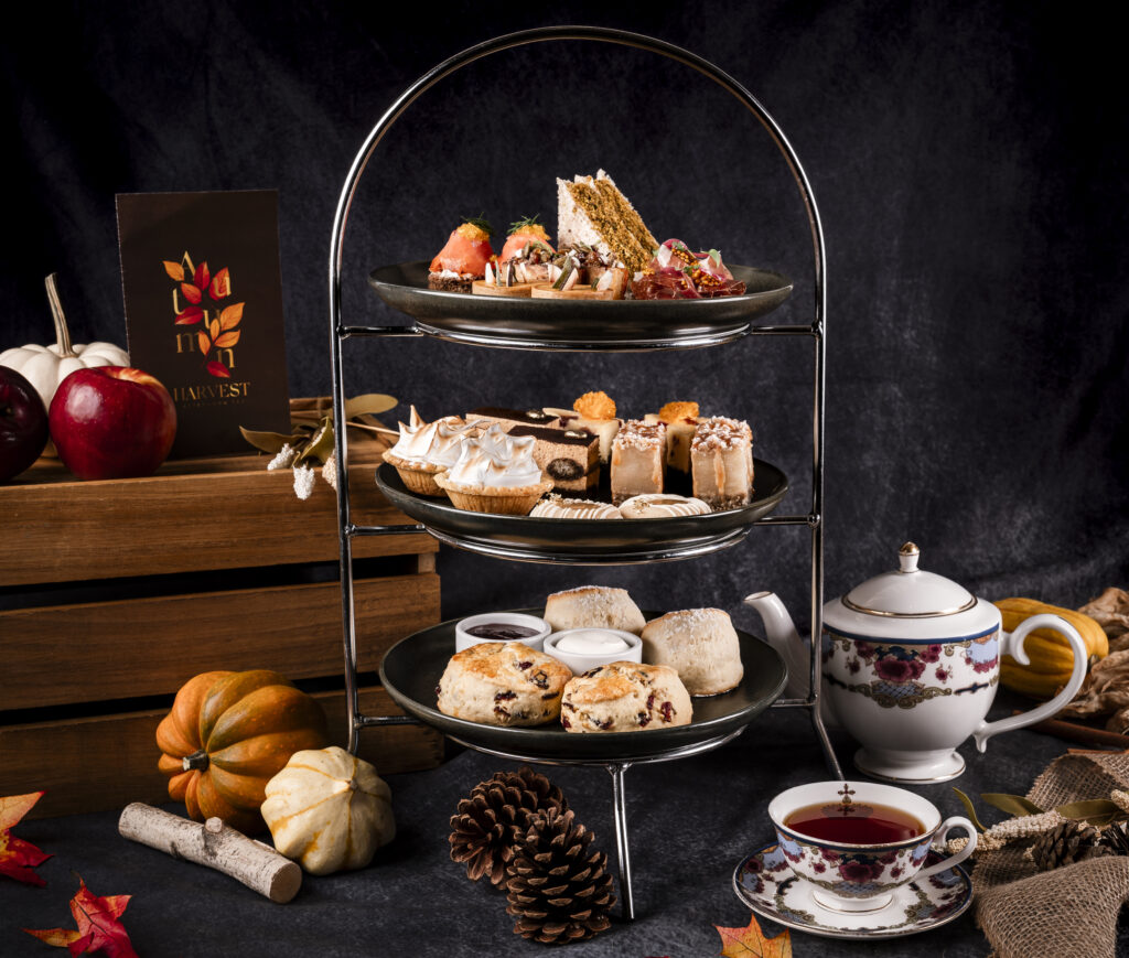 A three-tiered tea setting with cakes and other delicacies surrounded by autumnal gourds. 