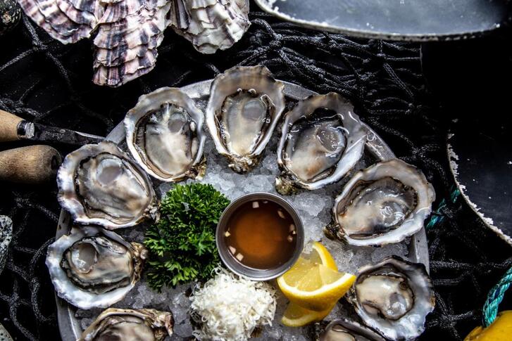 A platter of oysters over ice with dips and lemon wedges