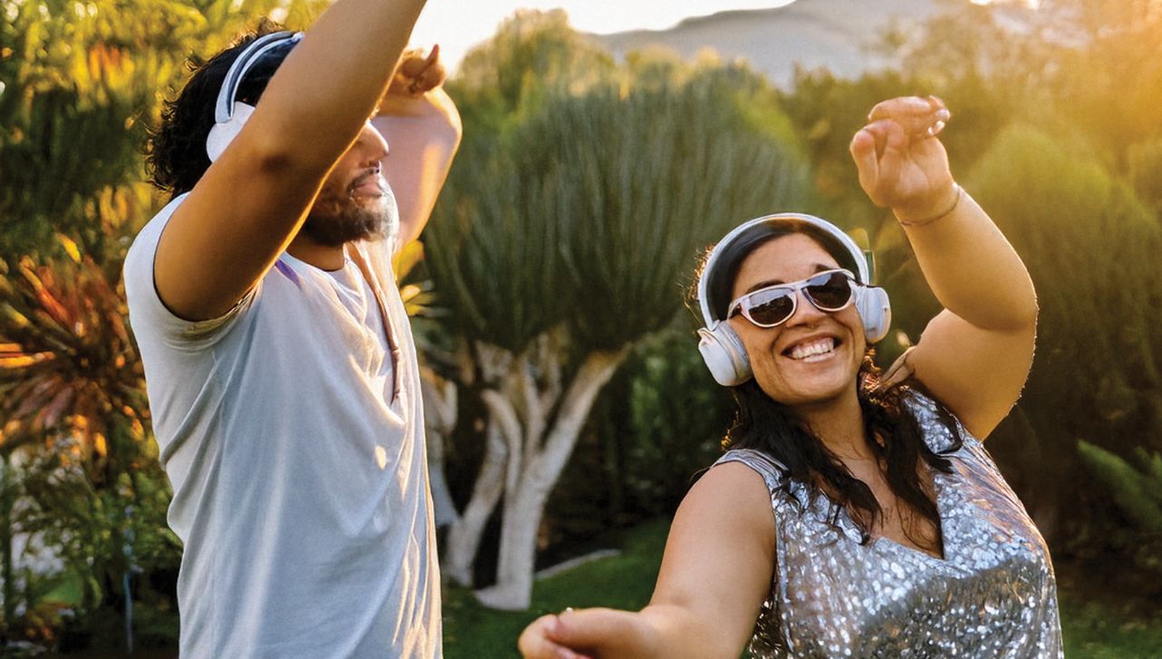 Two people wearing headphones dancing outside.