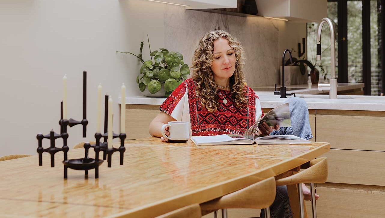 karri green-schuermans sits at her dining table at home, reading a magazine