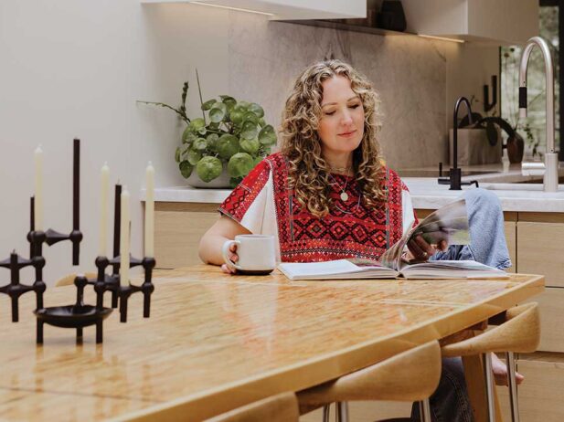 karri green-schuermans sits at her dining table at home, reading a magazine