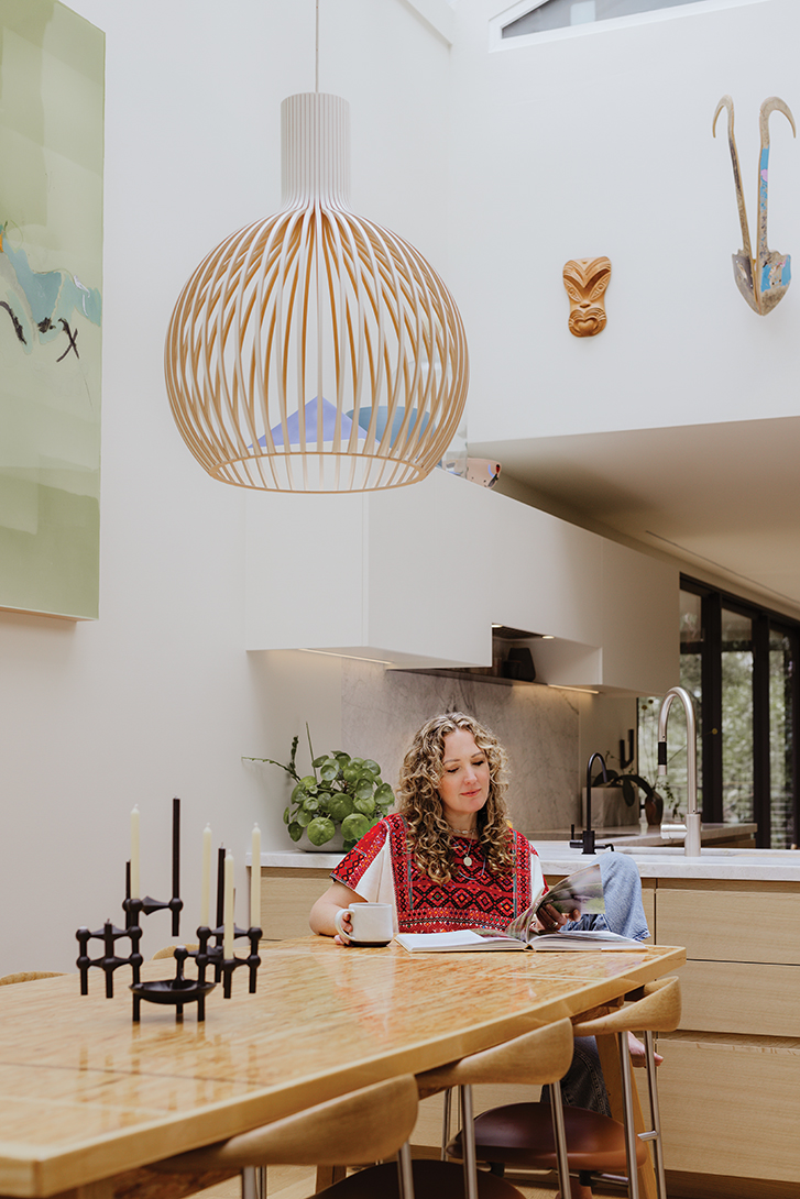 karri reads a magazine at a wooden dining table in her home.