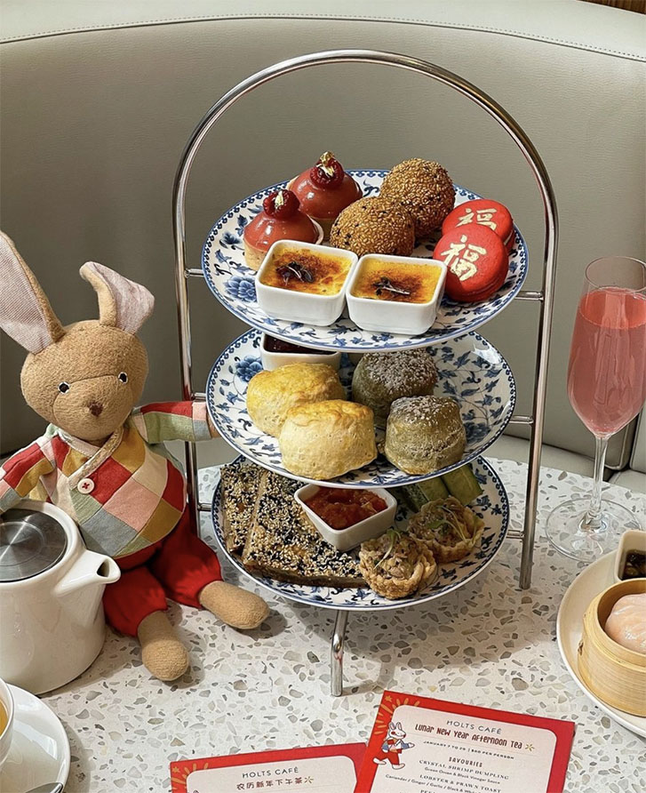 Sweets on a high tea tower with rabbit doll next to it.