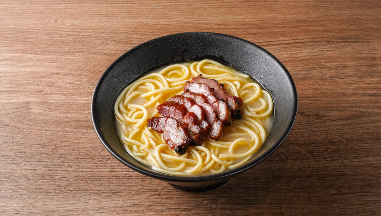 A bowl of thick noodles and BBQ pork