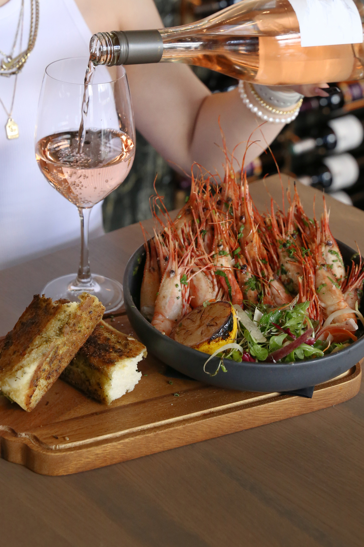 Prawns tail up on a wooden board with bread and rose.