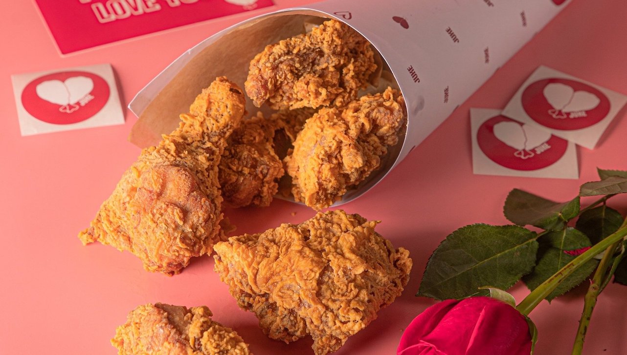 Pieces of chicken spilling out of a bouquet wrapping against a pink background.