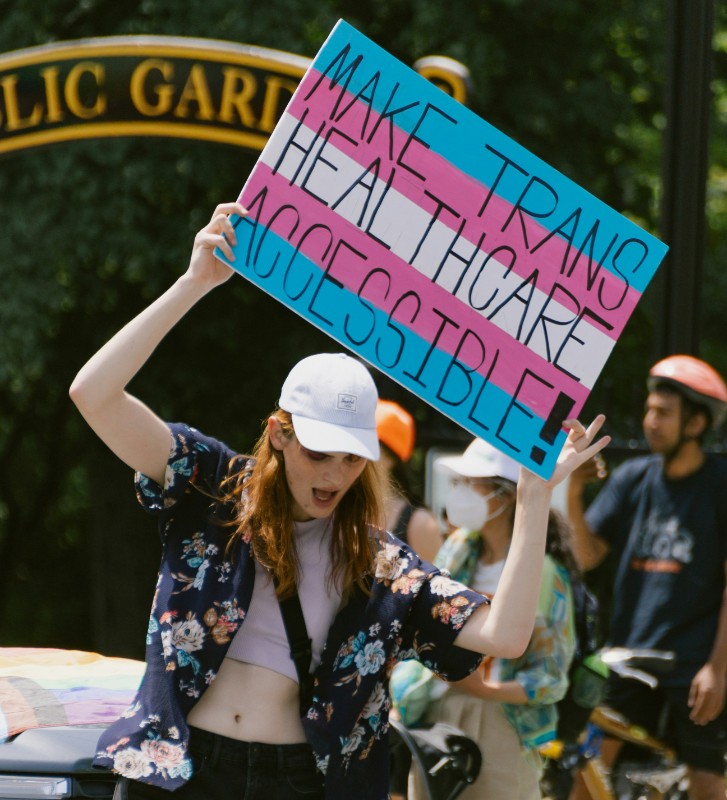 A Person during a Pride parade with a sign that says make Trans Healthcare Accessible!