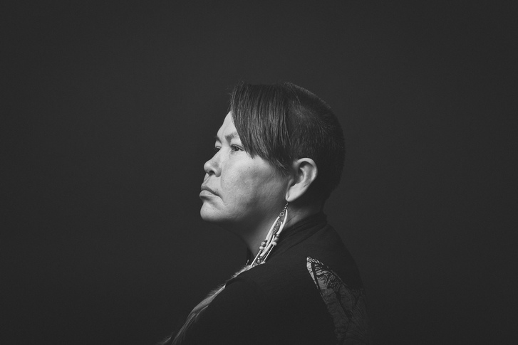A very stylized side profile, black and white portrait of an Indigenous woman against a black background.