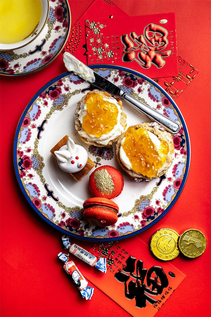 A plate at the centre with 2 red macarons, a rabbit dessert, and two jam desserts. Surrounded by red pockets and White Rabbit candies. 