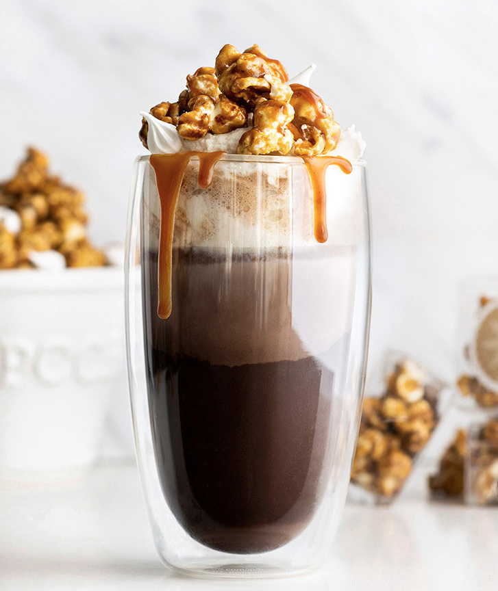 Clear mug of hot chocolate with whip cream and caramel dripping down glass