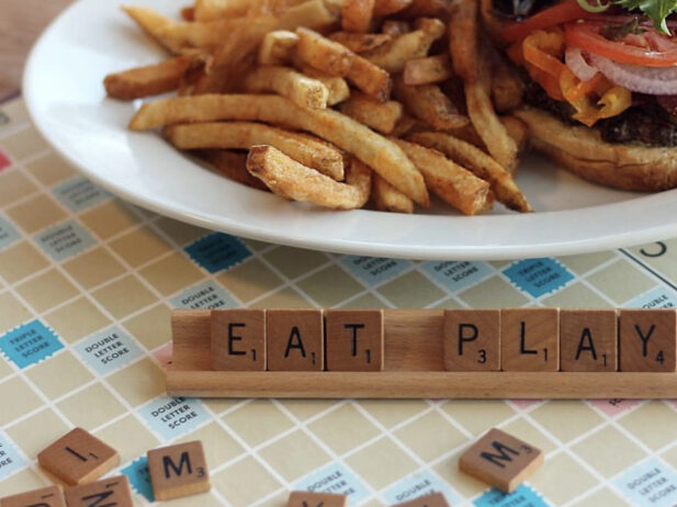 Scrabble tiles spelling "Eat Play" in front of a burger.