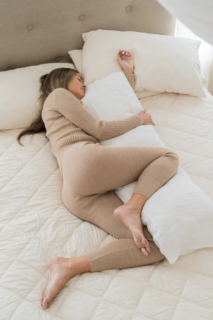 Woman with leg over a body pillow in bed
