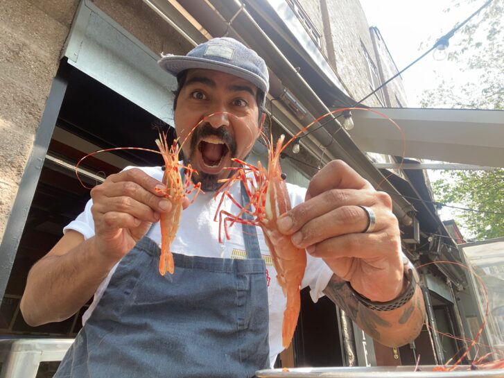 Chef holds two large prawns on the outside patio