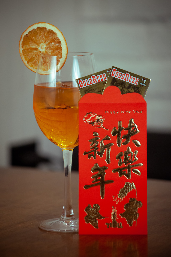 Orange coloured cocktail in wine glass next to a red envelope. 