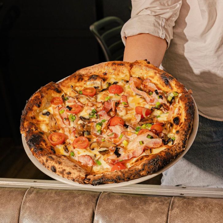 Pizza topped with pancetta, cherry tomatoes, mushrooms and green onions