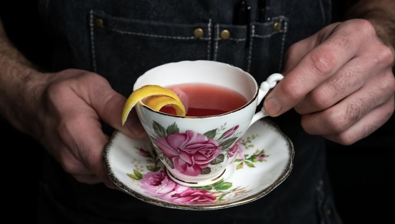 Hands holding a tea cup with red coloured drink inside.