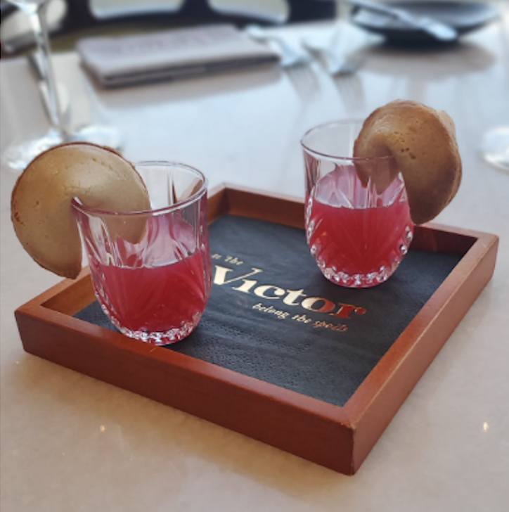 Two red coloured cocktails garnished with a fortune cookie. 