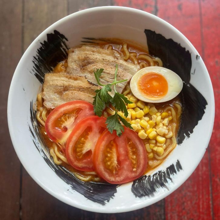 Bowl of tomato and garlic ramen topped with fresh tomato, corn, soft boiled egg and chashu