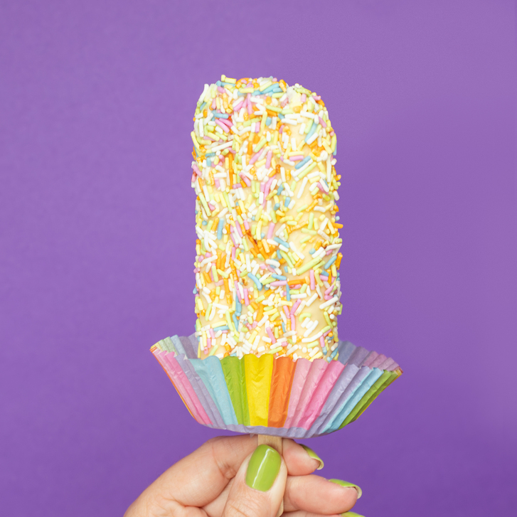 A hand holding the Ultimate Pride Bar coated with sprinkles, a product sold to raise funds for LGBTQ+ causes during Pride Month.