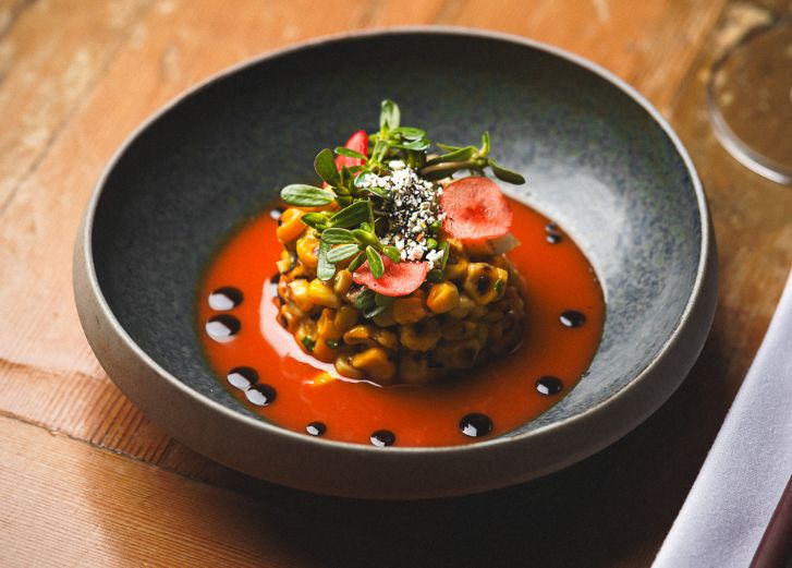 Grey bowl filled with pasta with a red sauce topped with leafy greens and a red flower garnish. 