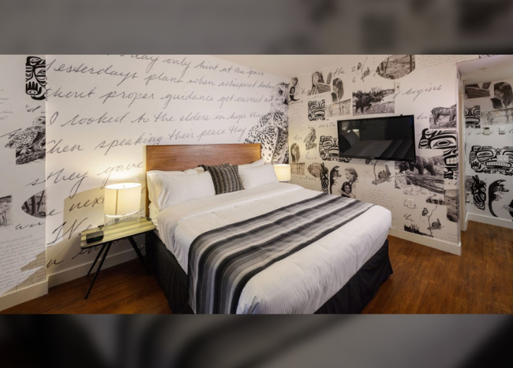 Bedroom with brown headboard and white and black bedding. TV on side wall. 