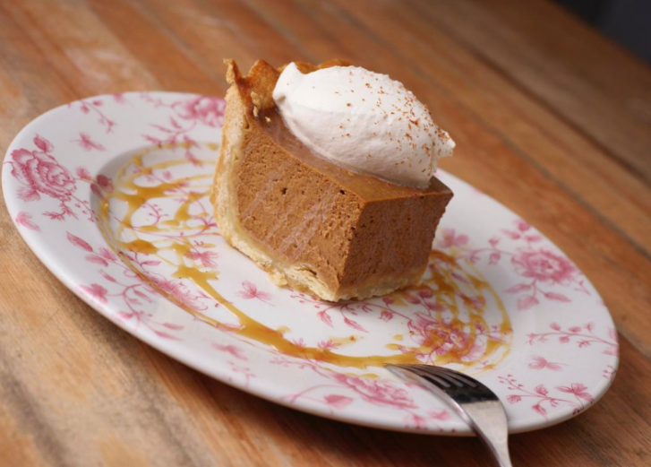 Pumpkin pie with whipped cream on pink and white speckled plate. 
