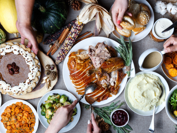 Full thanksgiving spread with turkey, mashed potatoes, pie, vegetables. Hands serving the dishes.