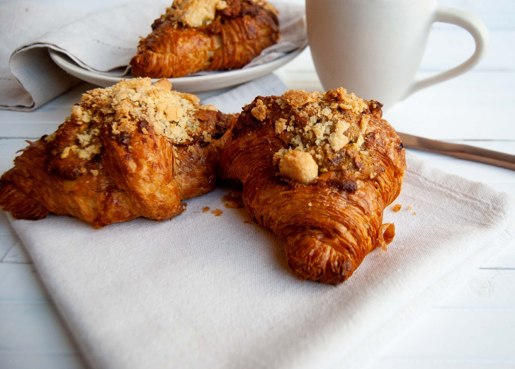 Two Croissants on white napkin with coffee mug and spoon in background. 