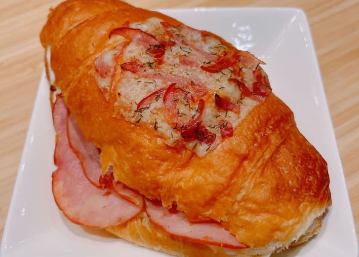 Stuffed croissant with ham on a white plate. 