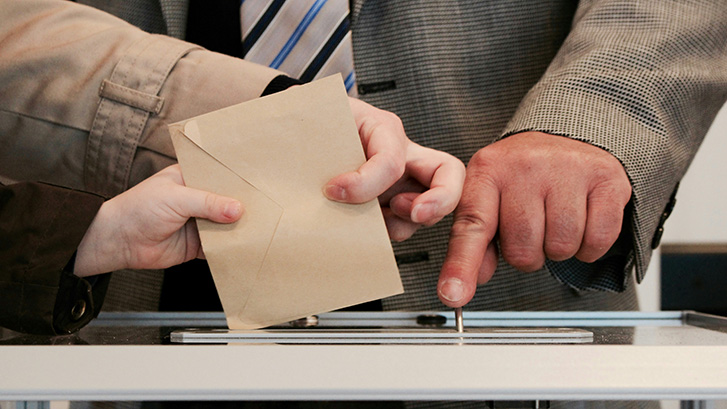 people putting a ballot into a voting box