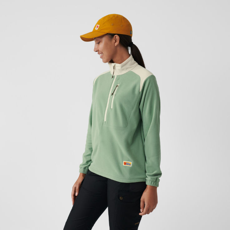 a happy woman in a hat is wearing a green and white sweatshirt that zips up